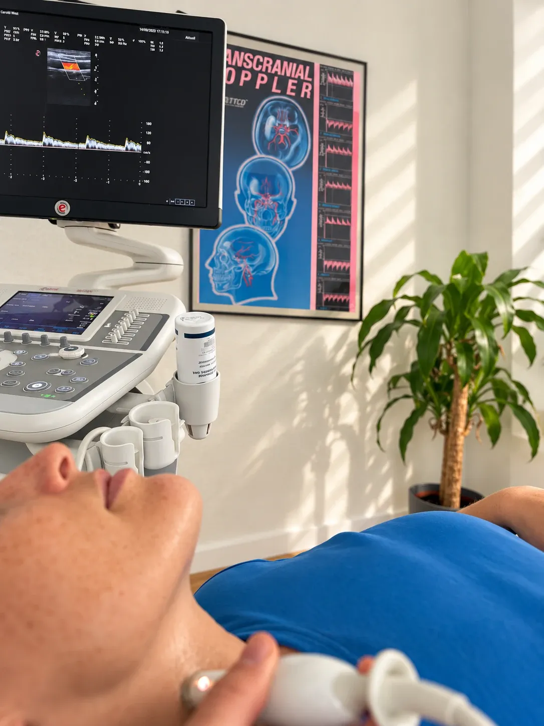 Ultraschall der Halsschlagader: Patientin liegt, im Hintergrund das Gerät mit Farbduplex-Bild auf dem Monitor